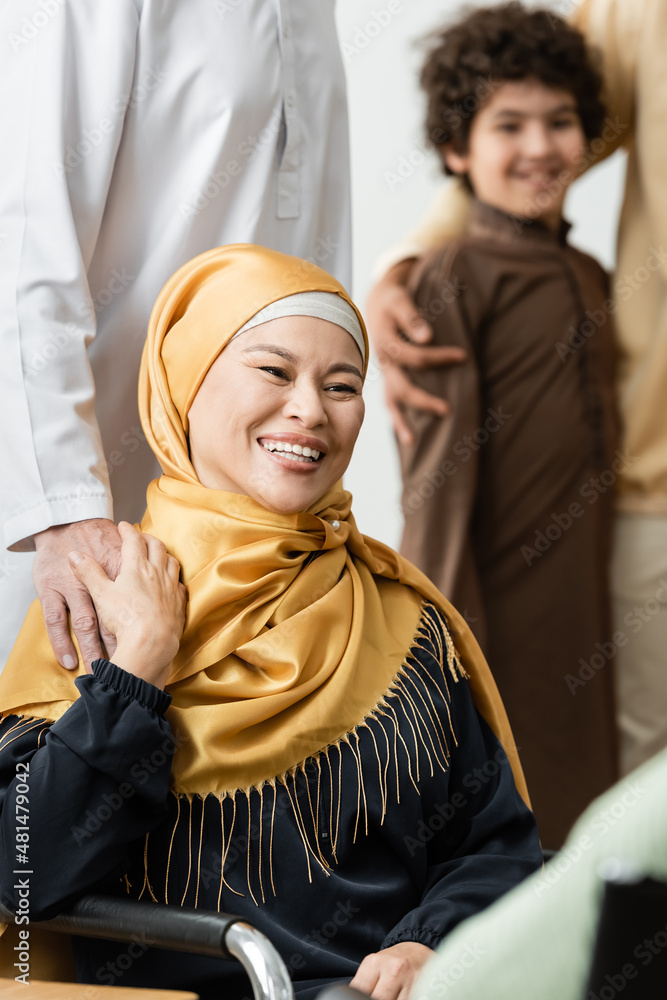 muslim asian woman in hijab smiling near husband and blurred arabian grandson.