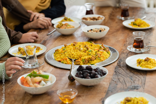 cropped view of muslim family near table served with pilaf, dates, baklava, tea and honey.