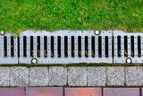 gray grating of the drainage system for drainage of rainwater in the park at the edge of the sidewalk from a stone tile with a green lawn, landscaping a city garden close-up top view, nobody.