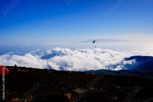 Paragliding above mountain peaks and white clouds during winter blue sunny day. © Joaquin Corbalan