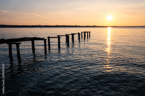 An old ramshackle pier with broken boards, during a beautiful sunset on a quiet lake.