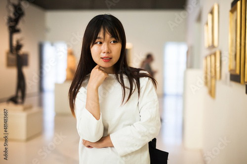 Serious chinese female visitor looking at artwork painting in the museum indoors