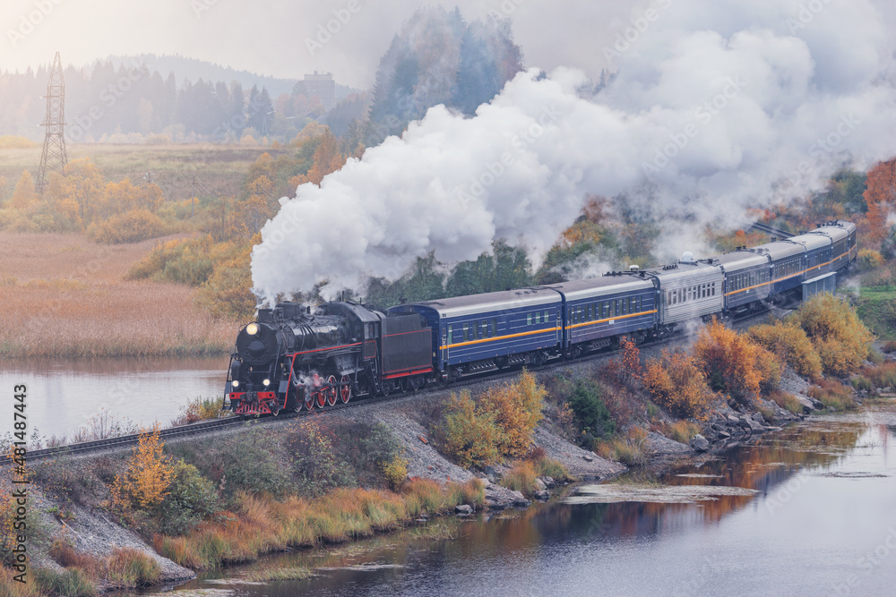 Retro steam train moves along the lake at autumn morning. Karelia. Russia. Retro steam train moves along the lake at autumn morning. Karelia. Russia.