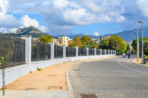 Fototapeta Naklejka Na Ścianę i Meble -  View of Mount Lycabettus Hill and the Plaka district from a street that runs along the fenced perimeter of the Kerameikos ancient cemetery in Athens, Greece.