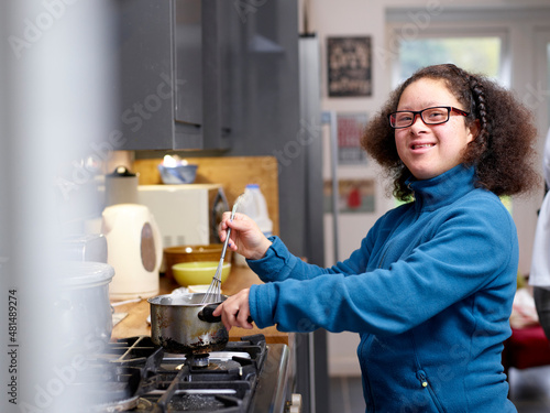 Quadro su tela Portrait of smiling girl  with Down Syndrome cooking in kitchen