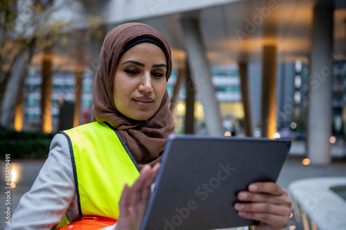UK, London, Female engineer in hijab and hardhat using digital tablet