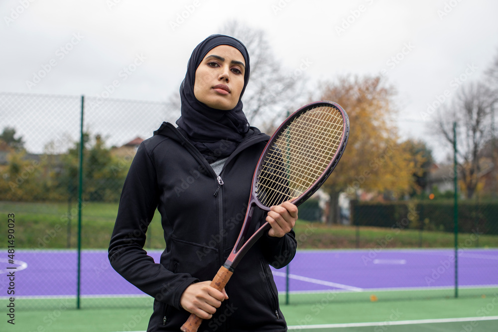 Portrait of woman in black sports clothing and hijab holding tennis racket  Photos | Adobe Stock