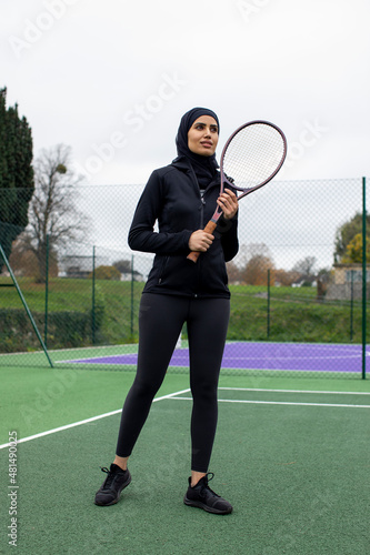Woman in black sports clothing and hijab holding tennis racket in tennis court © Cultura Creative
