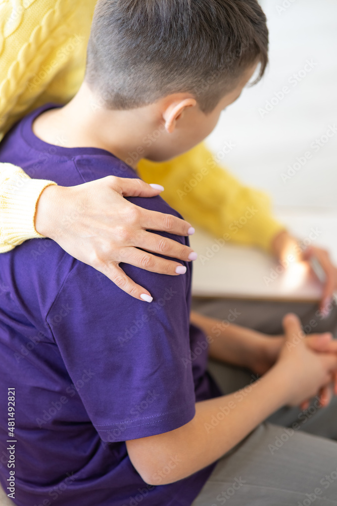 Close-up Hands of unrecognizable woman on shoulder of teenager. Woman psychologist in yellow sweater accepts teenager in ight cozy office. Gives him support and care by holding his shoulder. 