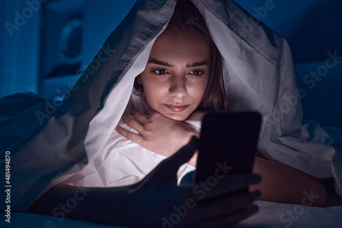 Female using smartphone under blanket