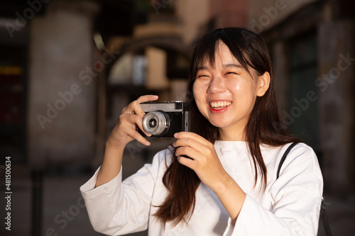 Smiling young girl holding camera in hands and photographing in city. High quality photo