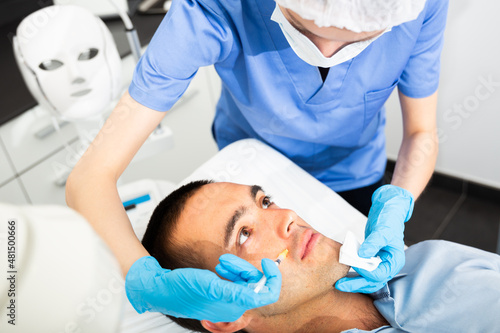 Woman doctor giving rejuvenating injections with syringe for facial correction to male patient in beauty clinic