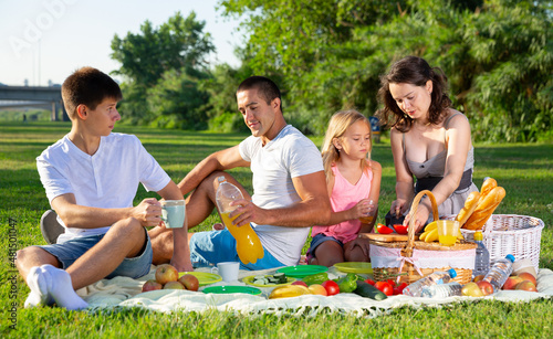 Happy parents with two kids having picnic together on green meadow in park. High quality photo © JackF