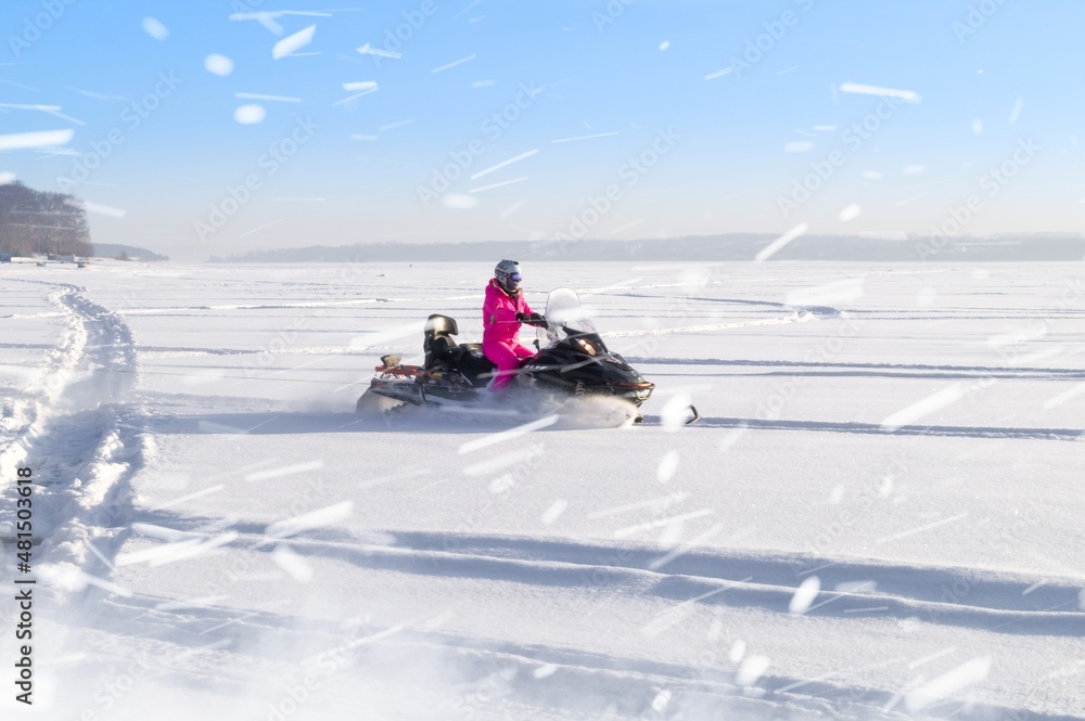 A girl rides a snowmobile through a snow-covered field. Riding on winter modes of transport. Active recreation. Snowmobiling in winter. Selective focus