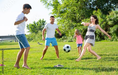 Positive parents with two kids playing soccer together on green field on summer day. High quality photo