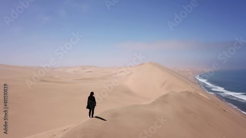 A young woman walks along sandy dunes on seashore. Sandwich Harbour in Namibia.