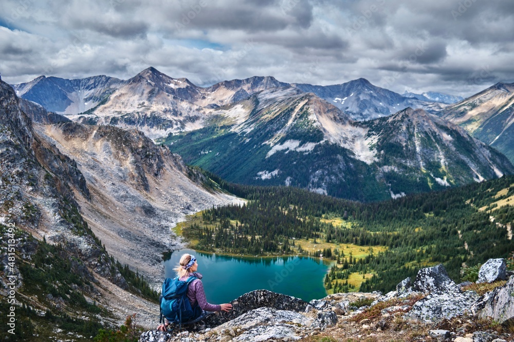 Woman backpacker sitting on cliff above the glacial lake enjoying the views of mountains. Blowdown lake in Stein Valley Heritage Park. Pemberton. British Columbia. Canada