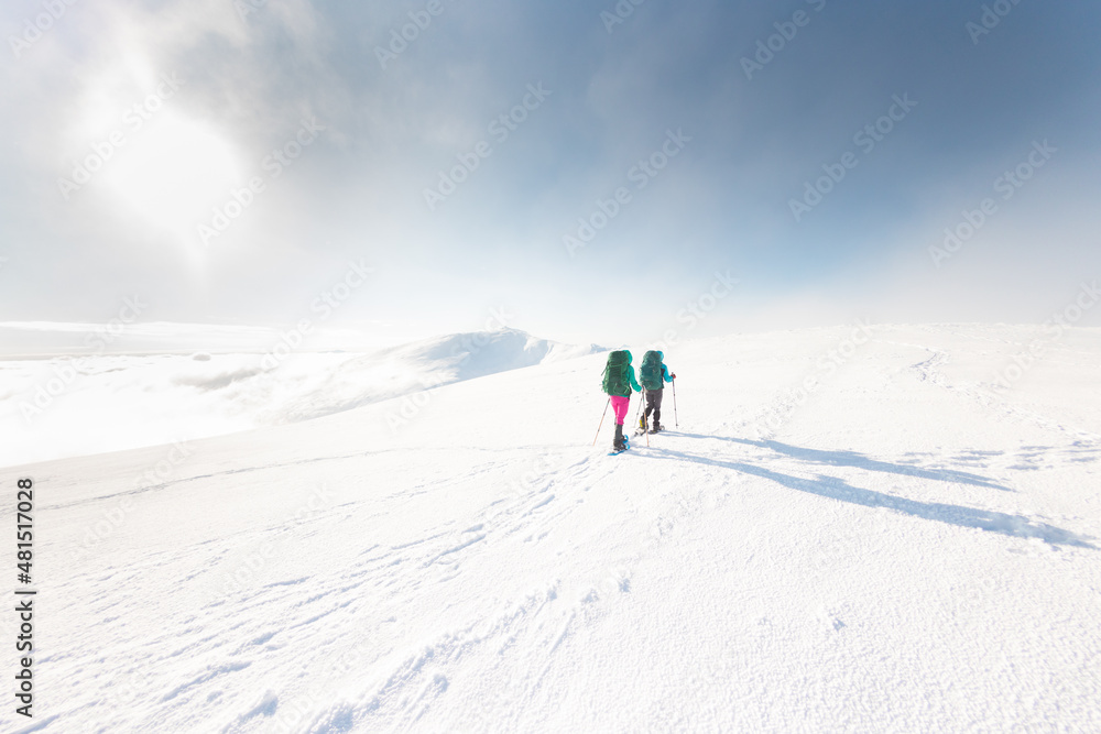 Two women walk in snowshoes in the mountains