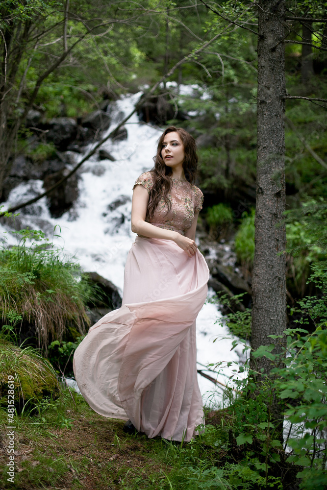 A young woman in a long dress on the background of a mountain waterfall. Enjoyment of nature.