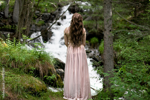A young woman in a long dress on the background of a mountain waterfall. Enjoyment of nature.