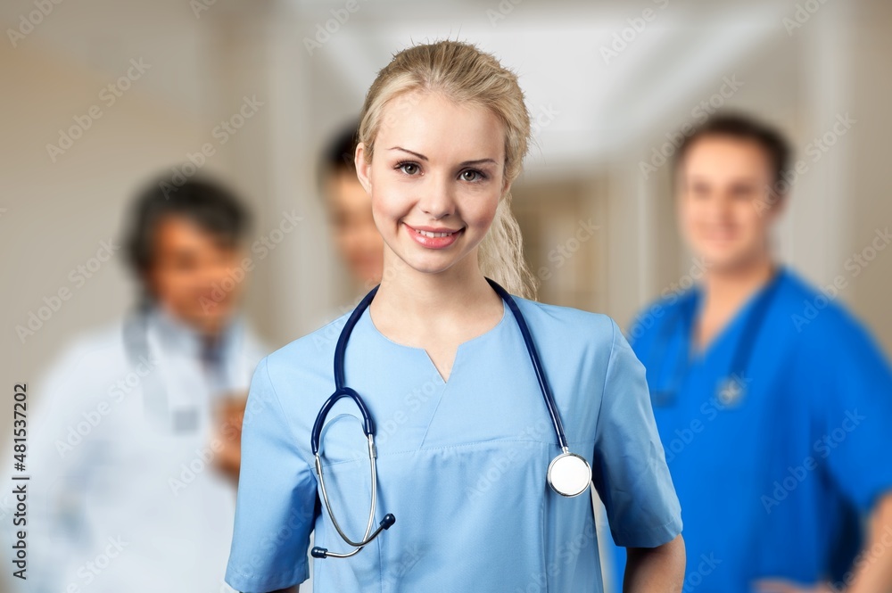 Portrait of happy young nurse in uniform with healthcare team in background. Successful doctor and nurses Portrait of happy young nurse in uniform with healthcare team in background. Successful doctor and nurses