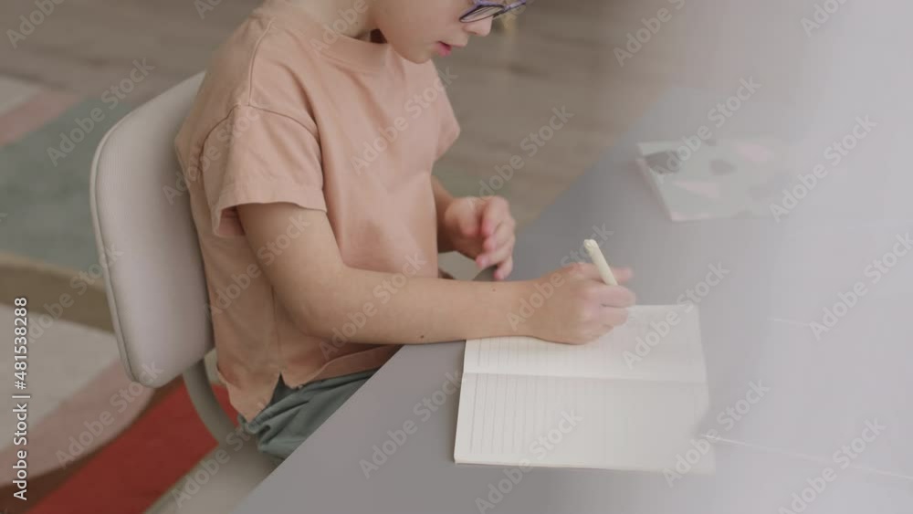 From-above slowmo shot of 11-year-old schoolgirl doing homework sitting by desk in her room From-above slowmo shot of 11-year-old schoolgirl doing homework sitting by desk in her room