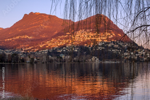 Monte Bre at the Lugano lake side at the golden hour time with orange tint reflection on water surface photo