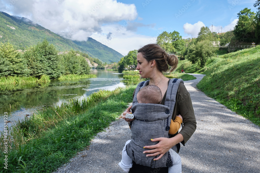 Caucasian mother with a baby carrier taking a walk around a lake in the middle of nature. healthy lifestyle
