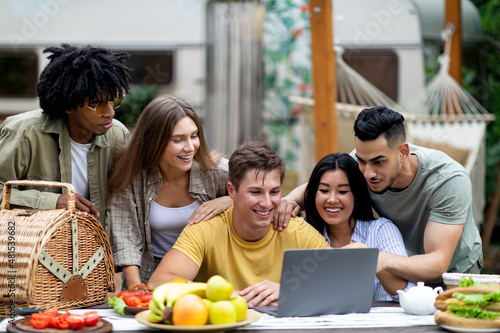 Group of multiracial millennial friends using laptop on autumn camping trip to countryside  chatting online  having fun