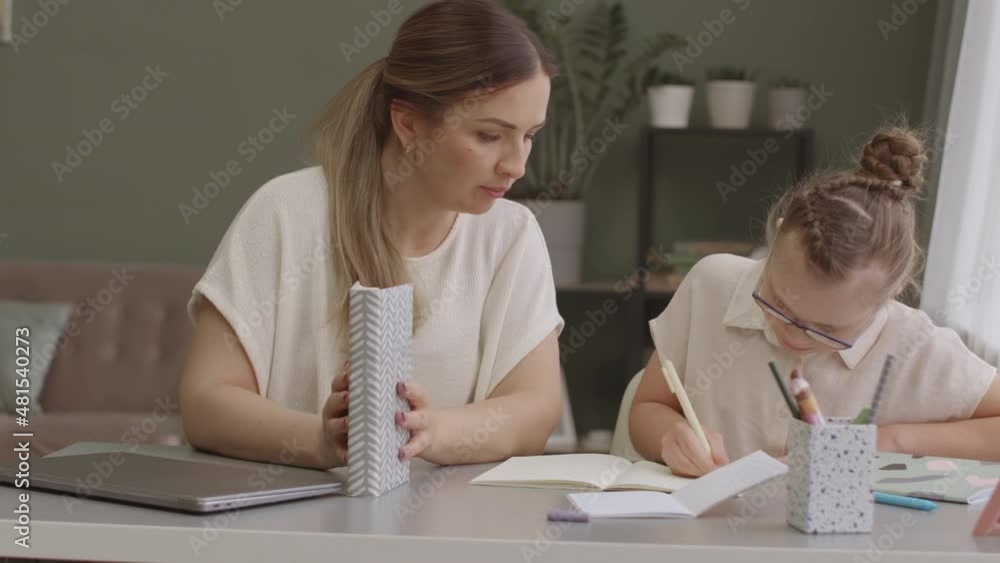 Medium slowmo shot of mom and daughter doing girls homework together sitting at desk in cozy living room Medium slowmo shot of mom and daughter doing girls homework together sitting at desk in cozy living room