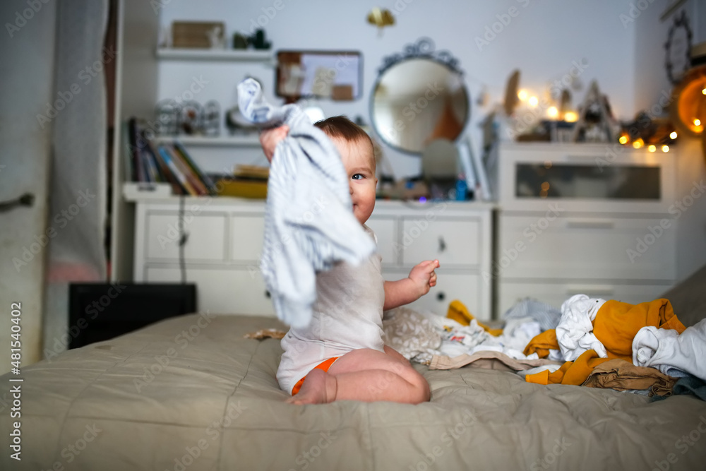 funny european chubby baby on the bed plays among the clothes, children's clothes and conscious consumption, 