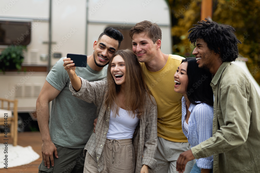 Obraz premium Happy multiracial friends taking selfie near their trailer, smiling and having fun together during autumn camping trip