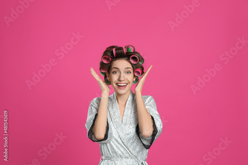Emotional young woman in silk bathrobe with hair curlers on pink background © New Africa