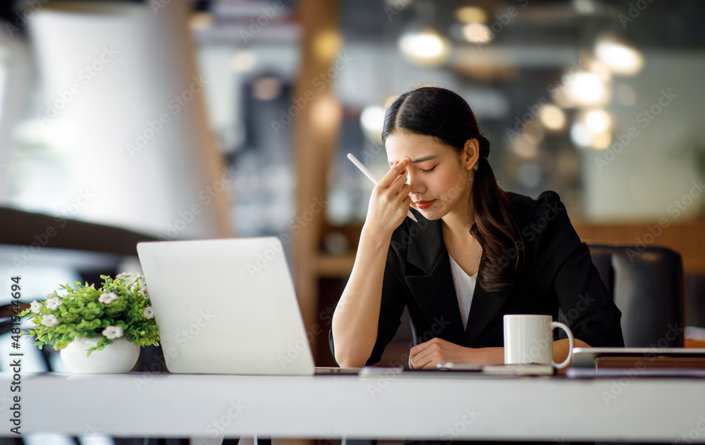 Asian women sitting in a home office With stress and eye strain.Tired businesswoman holding eyeglasses and massaging nose bridge. There are tablets, laptops, and coffee. Asian women sitting in a home office With stress and eye strain.Tired businesswoman holding eyeglasses and massaging nose bridge. There are tablets, laptops, and coffee.