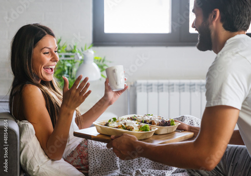 Tablou pe pânză Happy man bringing the breakfast to his girlfriend on the bed