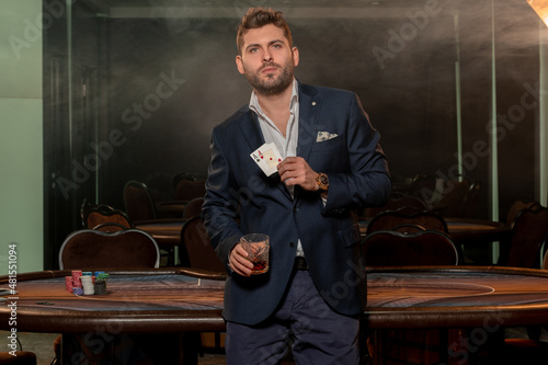 Young gambler with glass of drink and poker winning set of two aces standing in casino