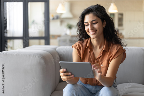 Portrait of smiling young woman using tablet, sitting on couch at home, copy space