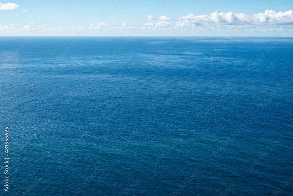 Clear and minimalistic panoramic seascape showing the endless blue waters of the Atlantic Ocean at the coast of Madeira under a sunny blue sky, also suitable as a maritime background texture