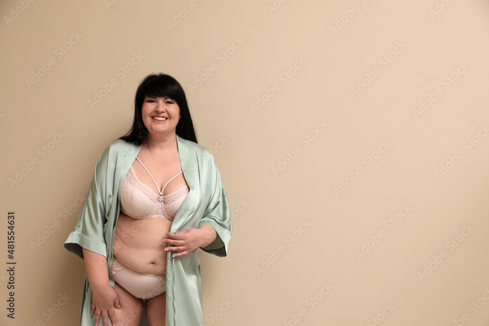Obraz premium Beautiful overweight woman in sexy underwear and silk robe on beige background, space for text. Plus-size model