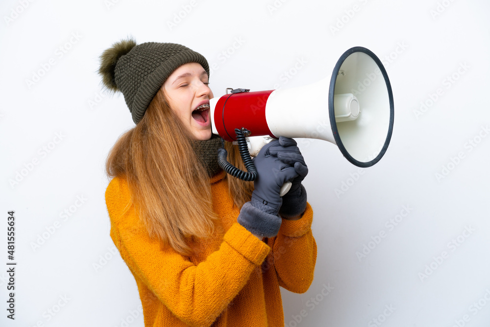 Teenager Russian girl wearing winter jacket isolated on white background shouting through a megaphone Teenager Russian girl wearing winter jacket isolated on white background shouting through a megaphone