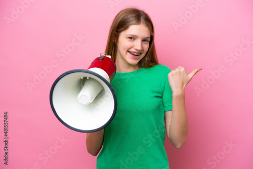 Teenager Russian girl isolated on pink background shouting through a megaphone and pointing side