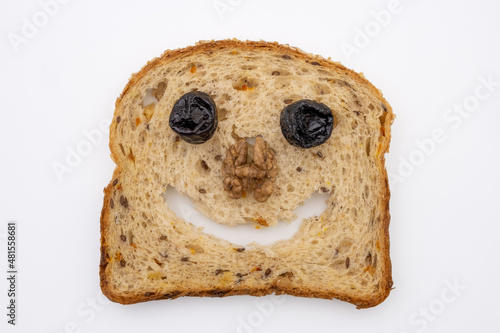 Funny face made from a slice of multigrain bread, dried plums and walnut. Joyful healthy food. Top view on white background.