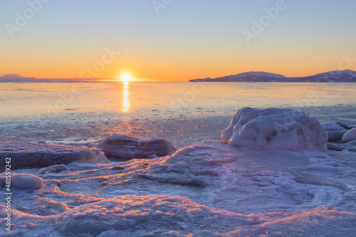 Winter seascape. Beautiful sunset. Ice-covered seashore and unfrozen water. Ice floes on the shore. Coast of the Sea of Okhotsk, Magadan region, Siberia, Far North of Russia. Cold weather. January.