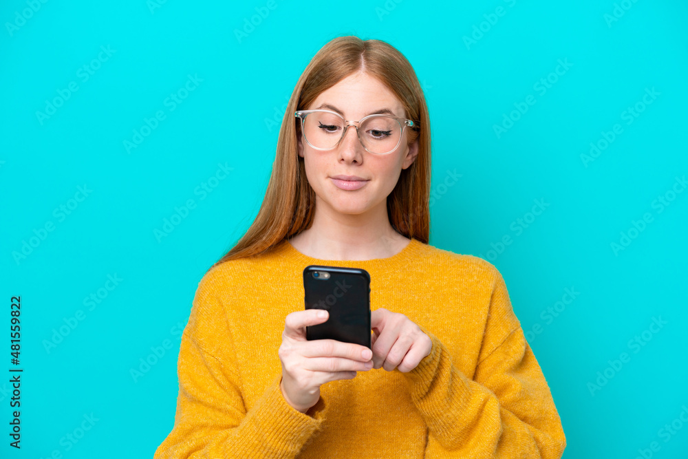 Young redhead woman isolated on blue background sending a message or email with the mobile Young redhead woman isolated on blue background sending a message or email with the mobile