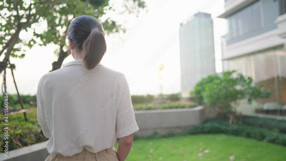 An asian casual woman calm alone walking with reading book against evening sunlight at condominium sky park, a green environment and modern high rise building in background, people and home hobby An asian casual woman calm alone walking with reading book against evening sunlight at condominium sky park, a green environment and modern high rise building in background, people and home hobby