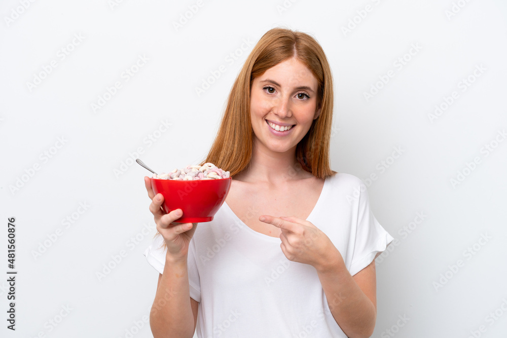 Young redhead woman holding a bowl of cereals isolated on white background and pointing it Young redhead woman holding a bowl of cereals isolated on white background and pointing it