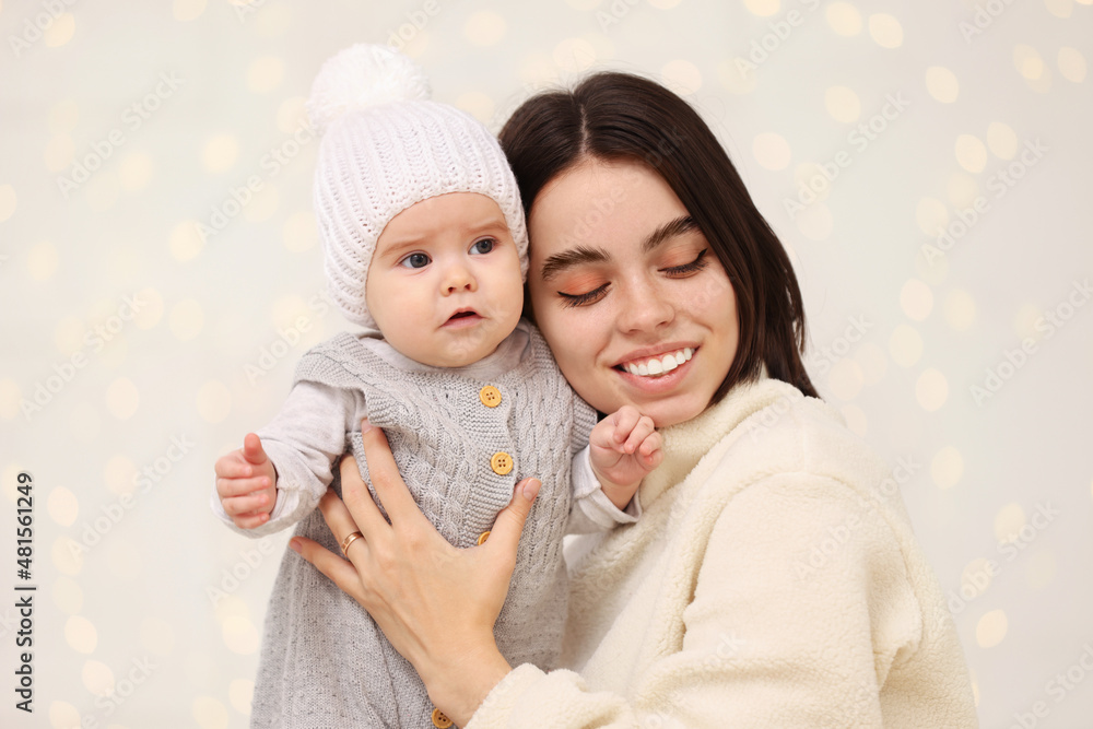 Happy young mother with her cute baby against blurred festive lights. Winter holiday Happy young mother with her cute baby against blurred festive lights. Winter holiday