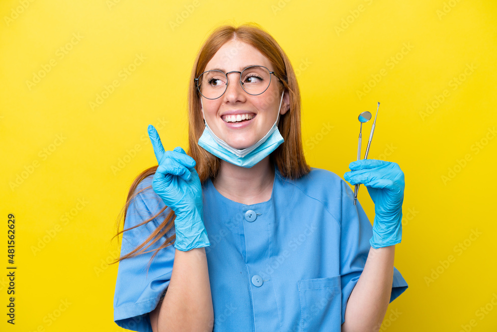 Young redhead Dentist woman isolated on yellow background pointing up a great idea Young redhead Dentist woman isolated on yellow background pointing up a great idea