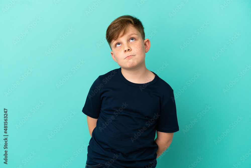Little redhead boy isolated on blue background and looking up Little redhead boy isolated on blue background and looking up