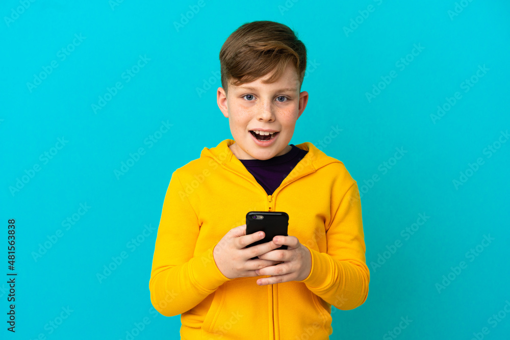 Little redhead boy isolated on blue background surprised and sending a message Little redhead boy isolated on blue background surprised and sending a message